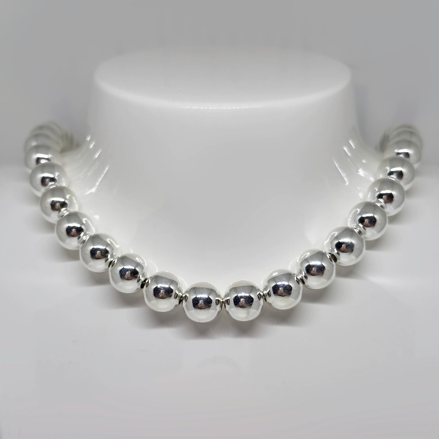 Hopeinen pallokaulakoru kuvattuna valkoisella korutelineellä