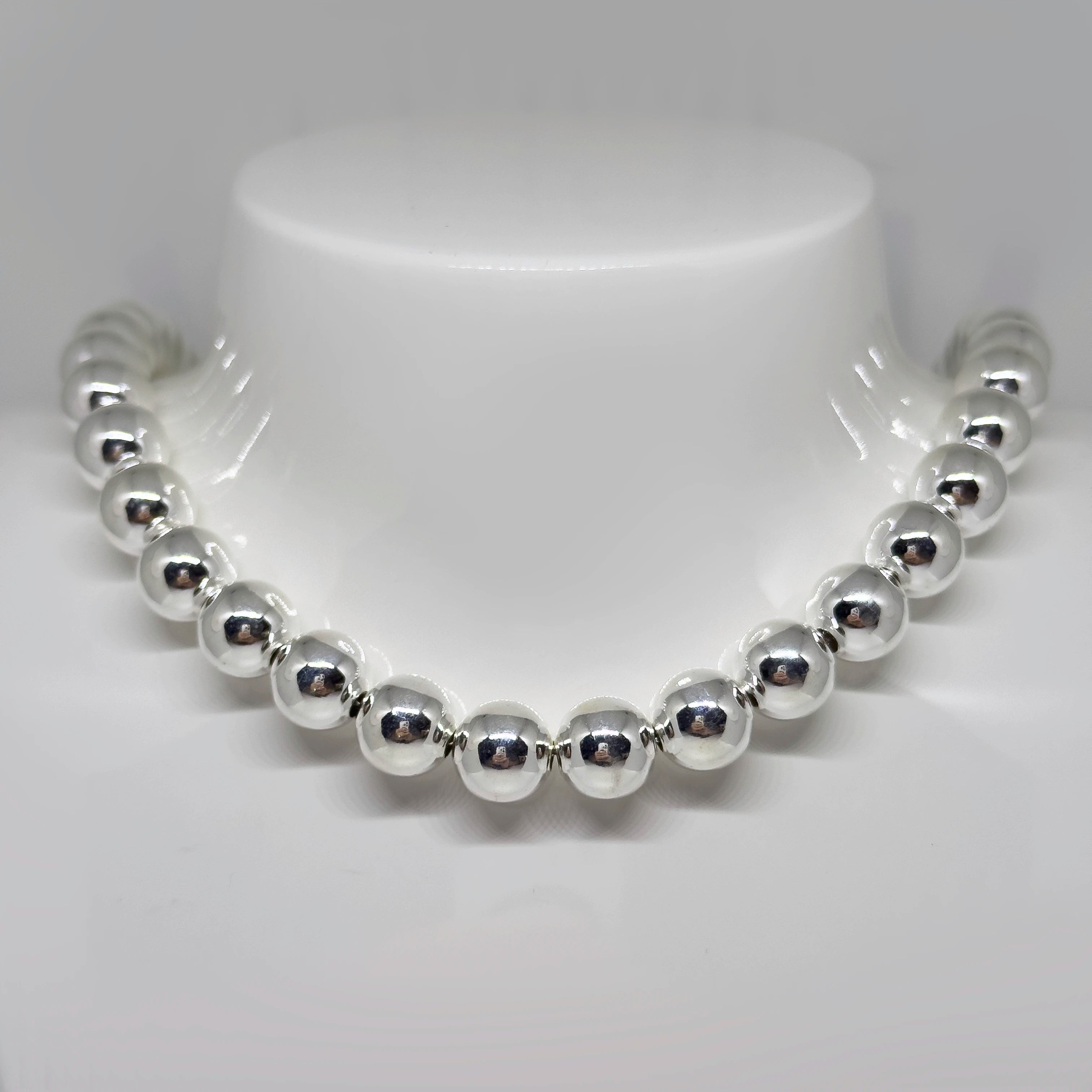 Hopeinen pallokaulakoru kuvattuna valkoisella korutelineellä