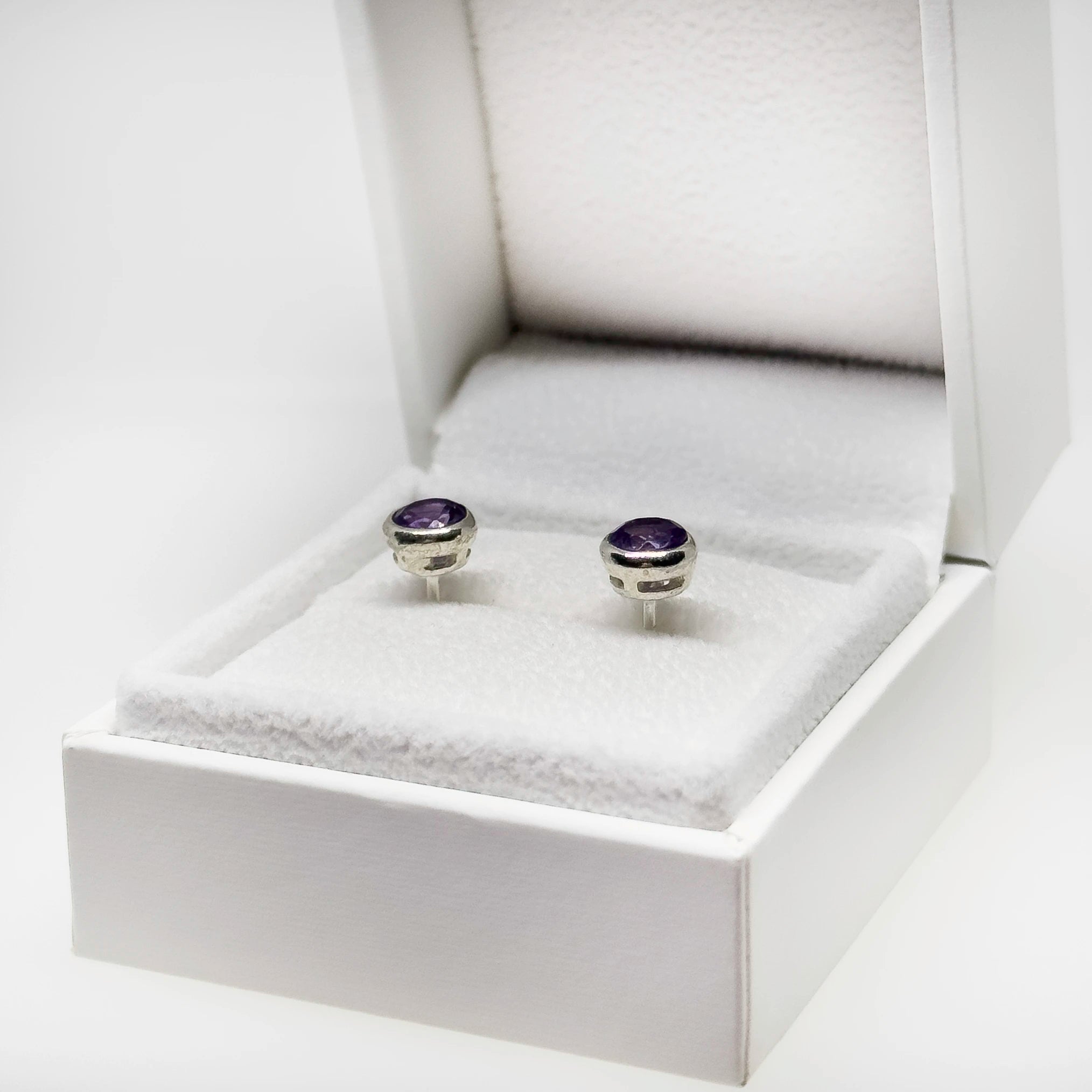 Hopeiset ametisti korvakorut kuvattuna valkoisella korutelineellä