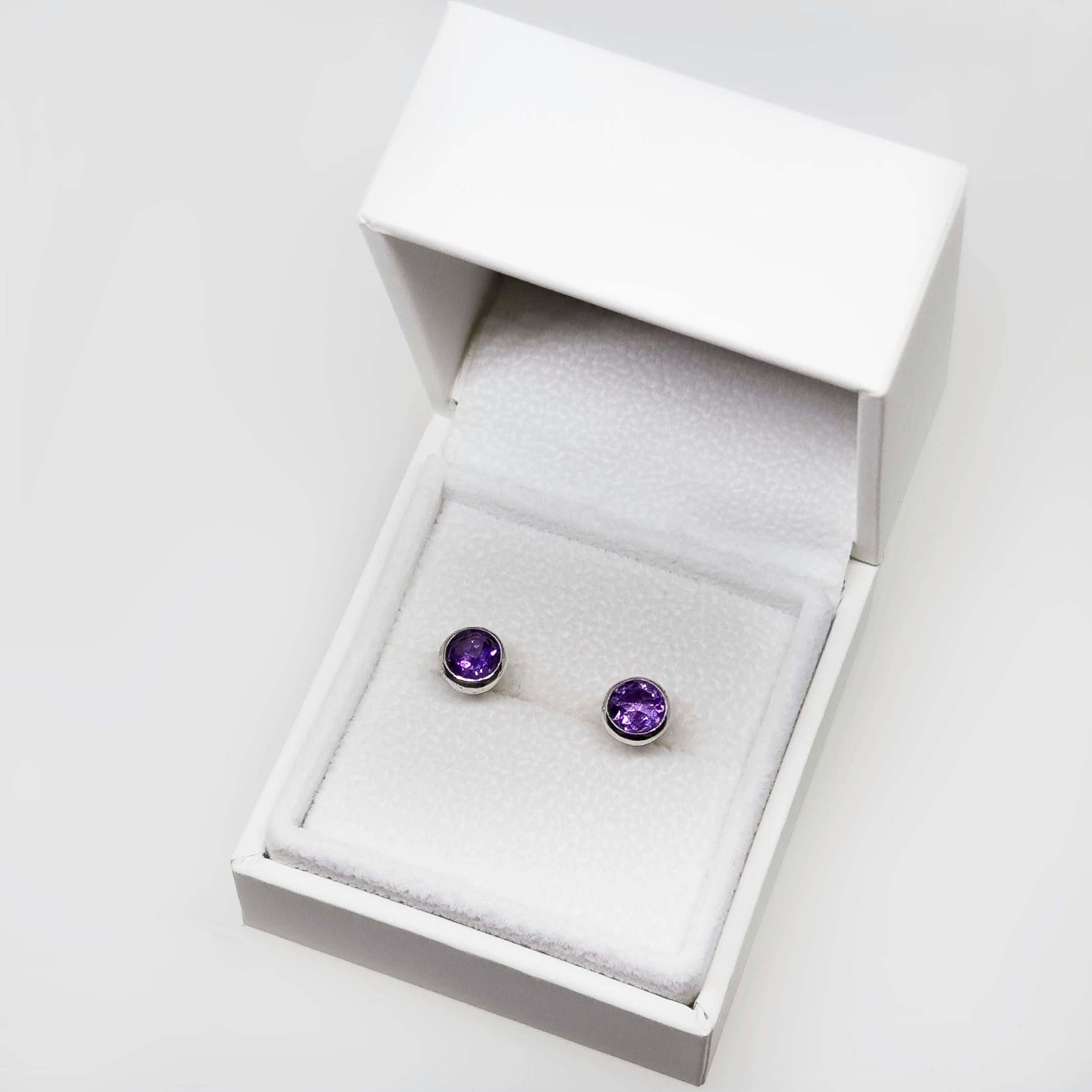 Hopeiset ametisti korvakorut kuvattuna valkoisella korutelineellä