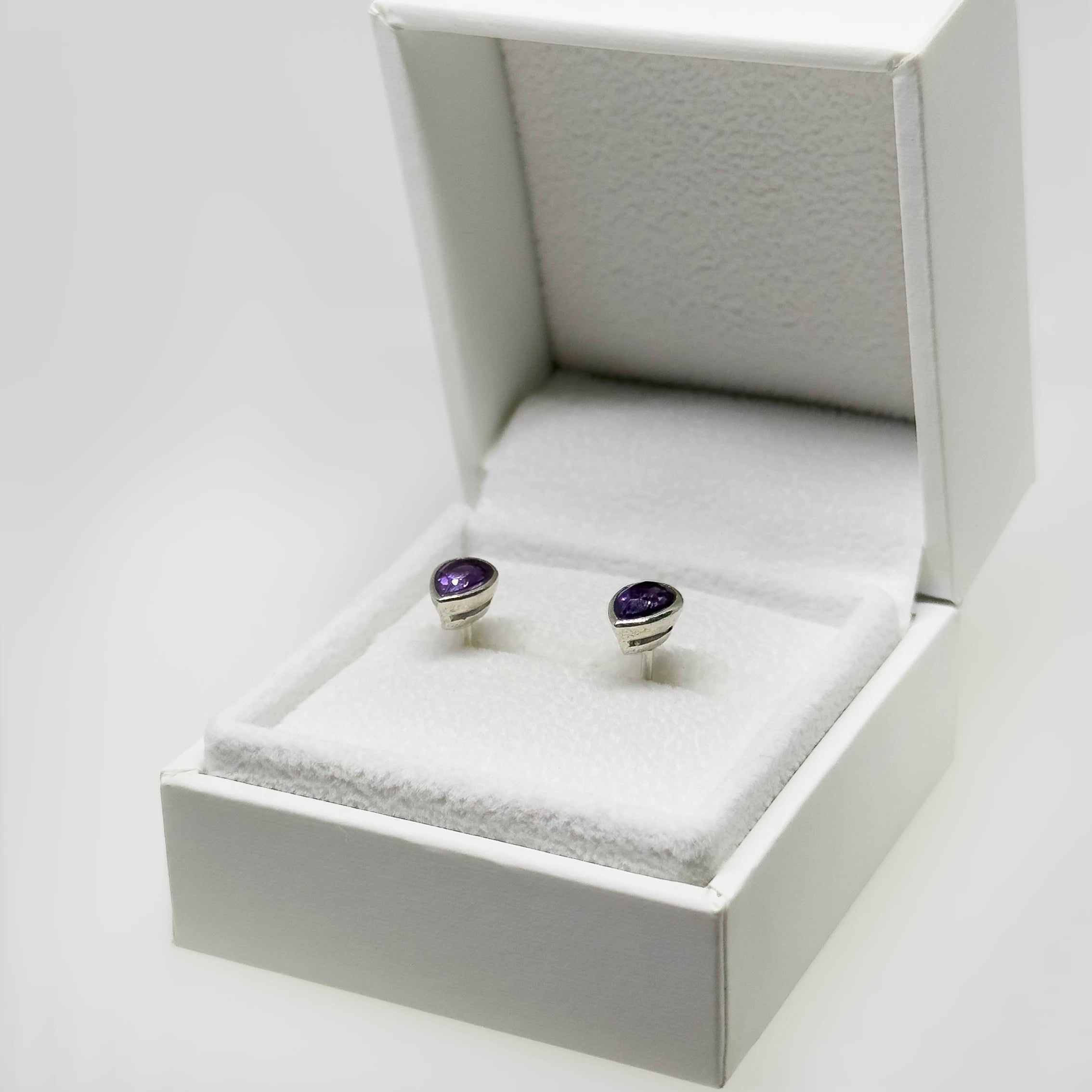 Hopeiset ametisti kyynel korvakorut kuvattuna valkoisella korutelineellä