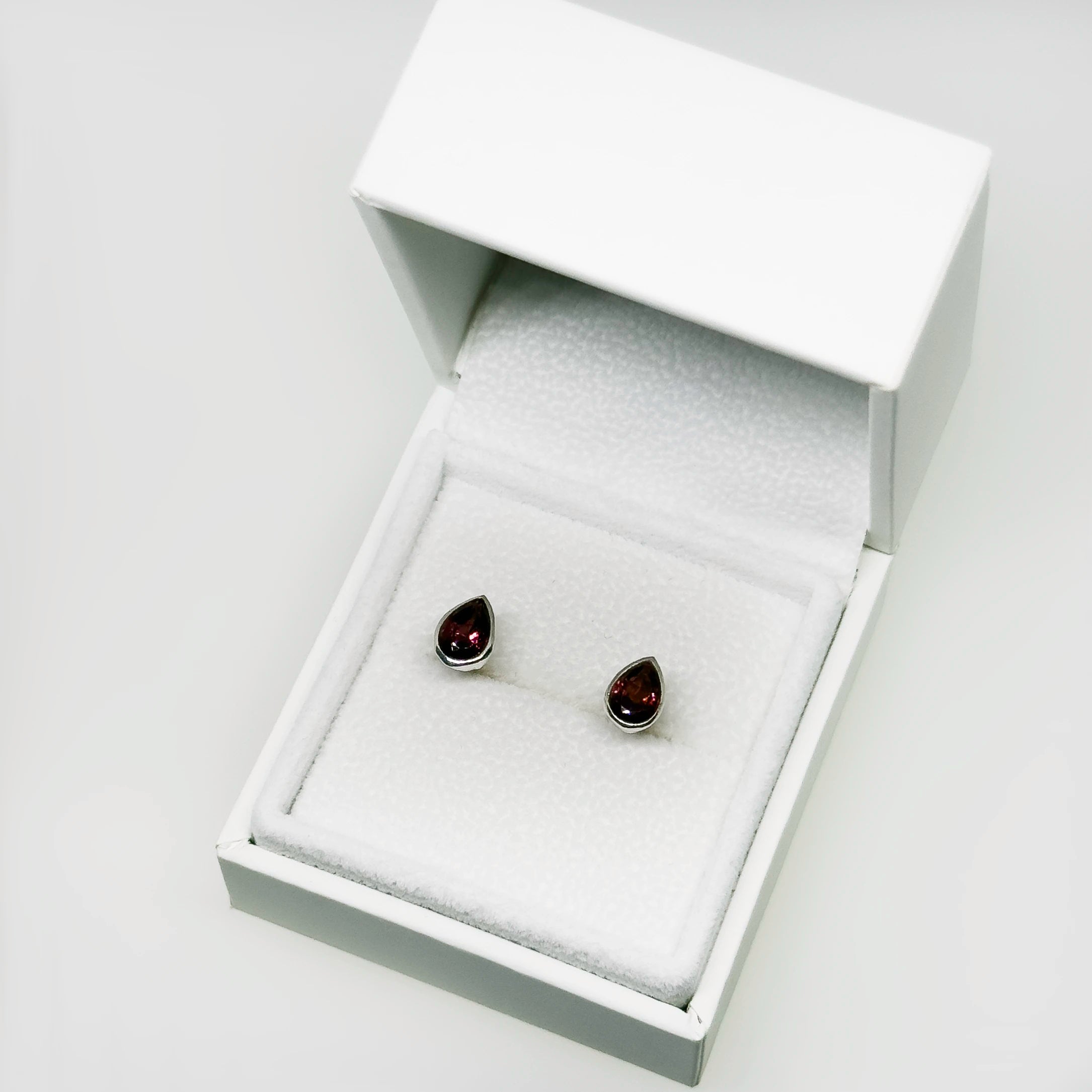 Hopeiset granaatti kyynel korvakorut kuvattuna valkoisella korutelineellä