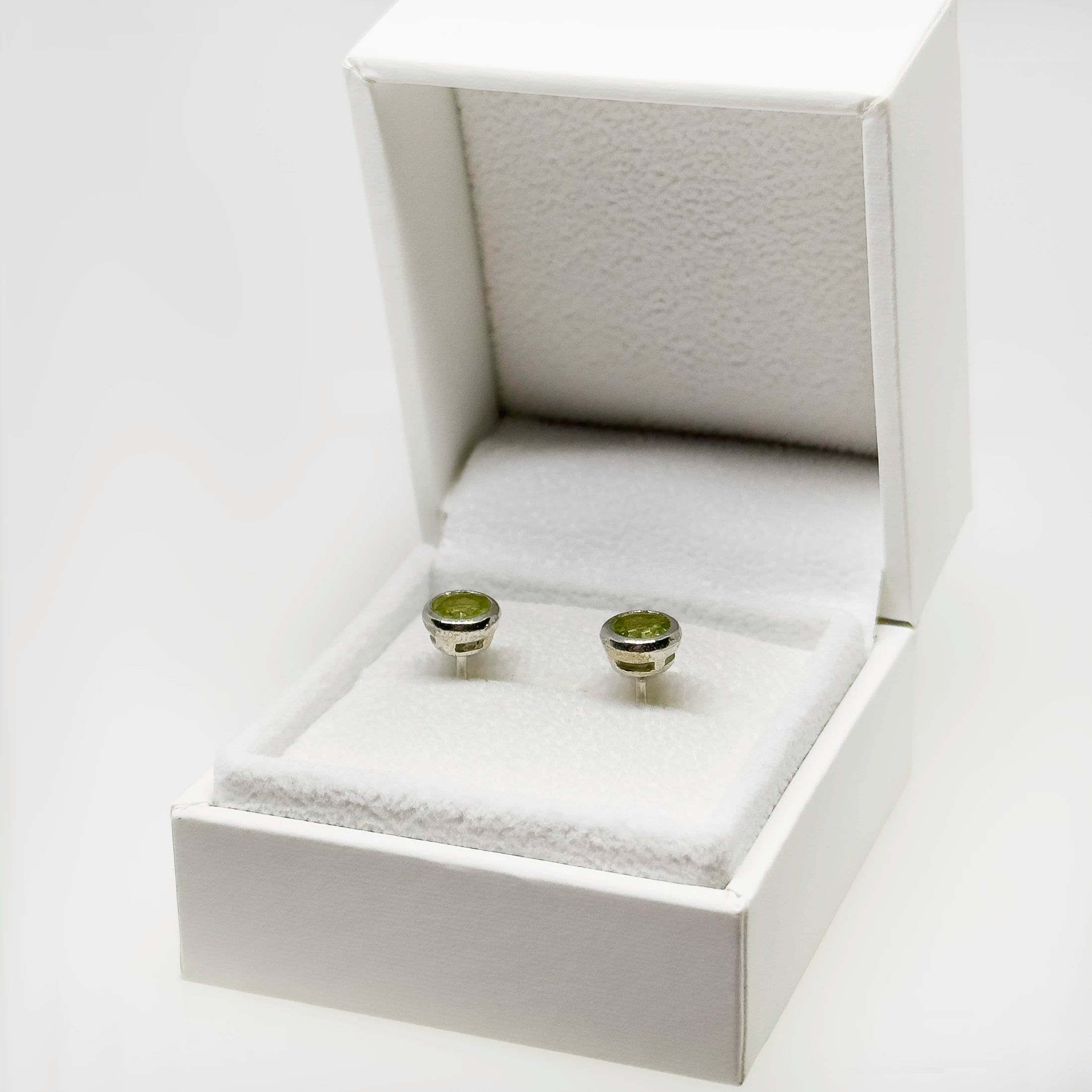 Hopeiset peridootti korvakorut kuvattuna valkoisella korutelineellä