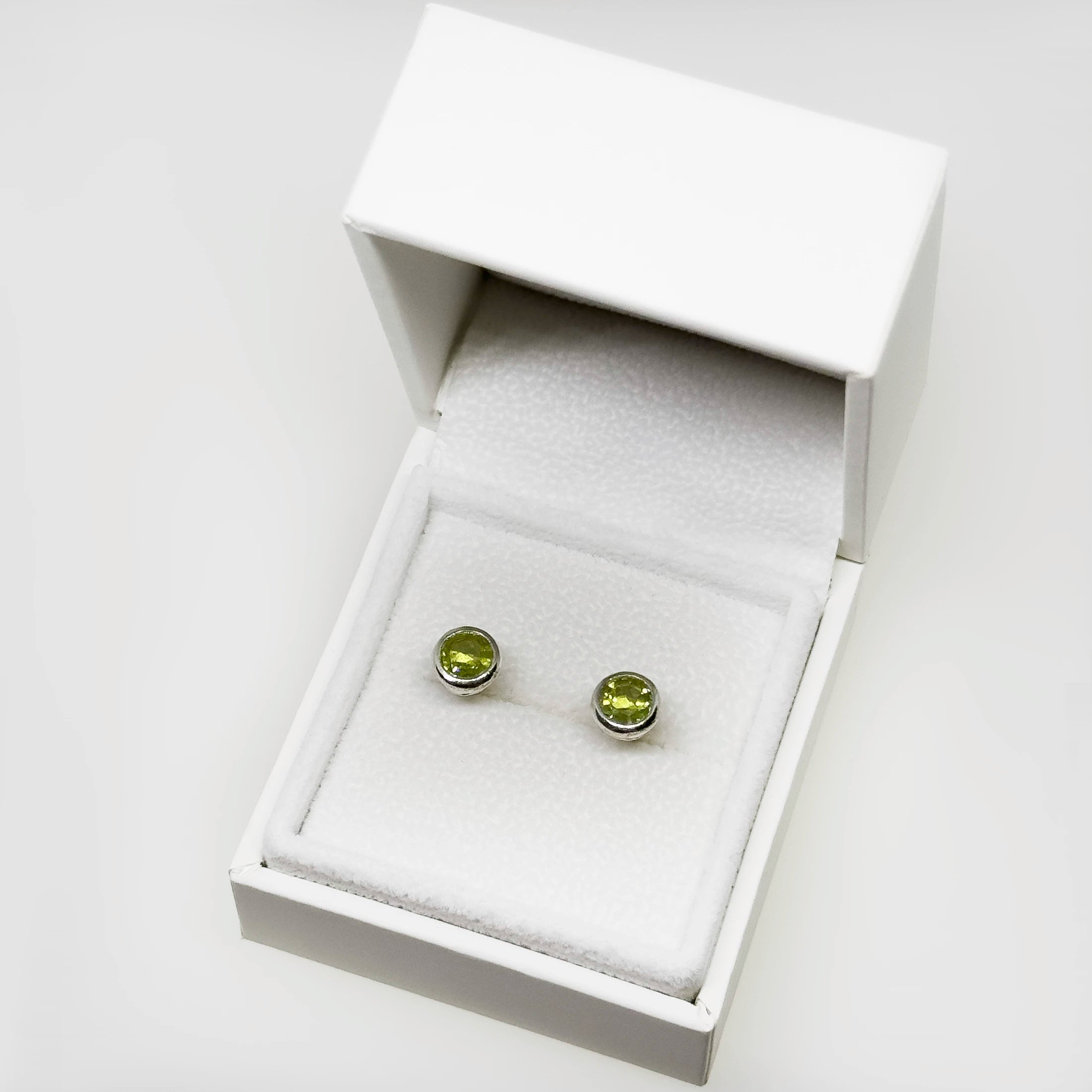 Hopeiset peridootti korvakorut kuvattuna valkoisella korutelineellä
