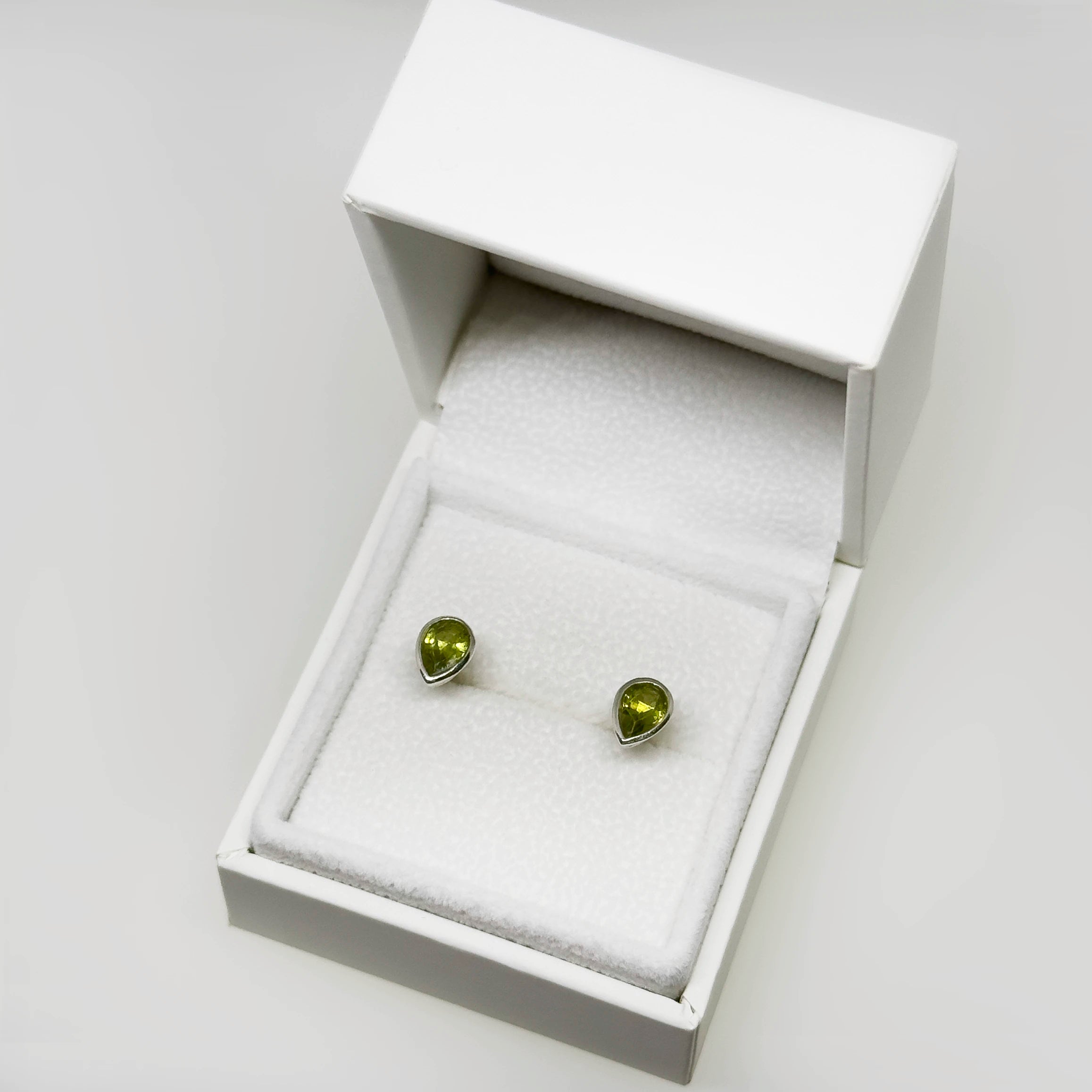 Hopeiset peridootti kyynel korvakorut kuvattuna valkoisella korutelineellä
