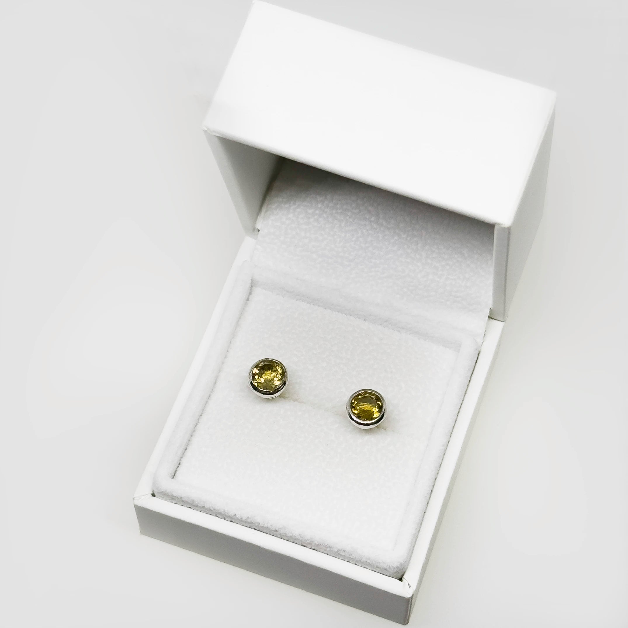 Hopeiset sitriini korvakorut kuvattuna valkoisella korutelineellä